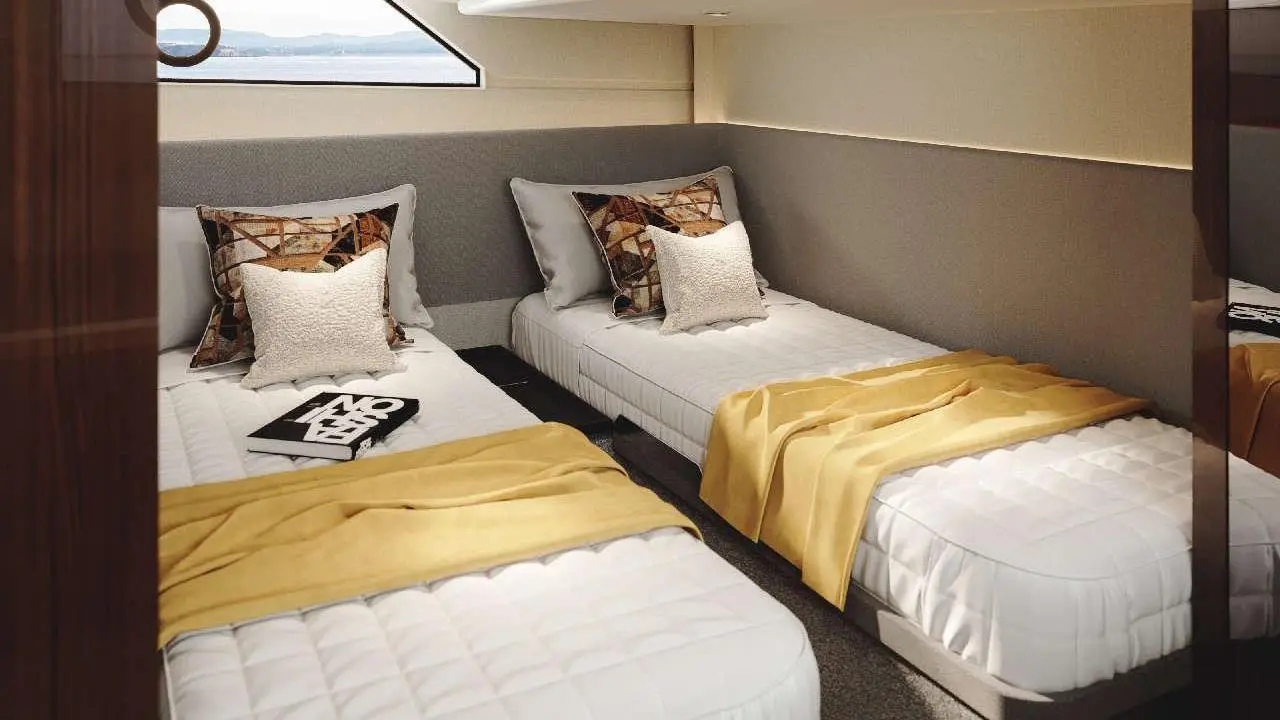 Modern boat cabin with two single beds, decorative pillows, yellow throws, and a view window showcasing the sea.